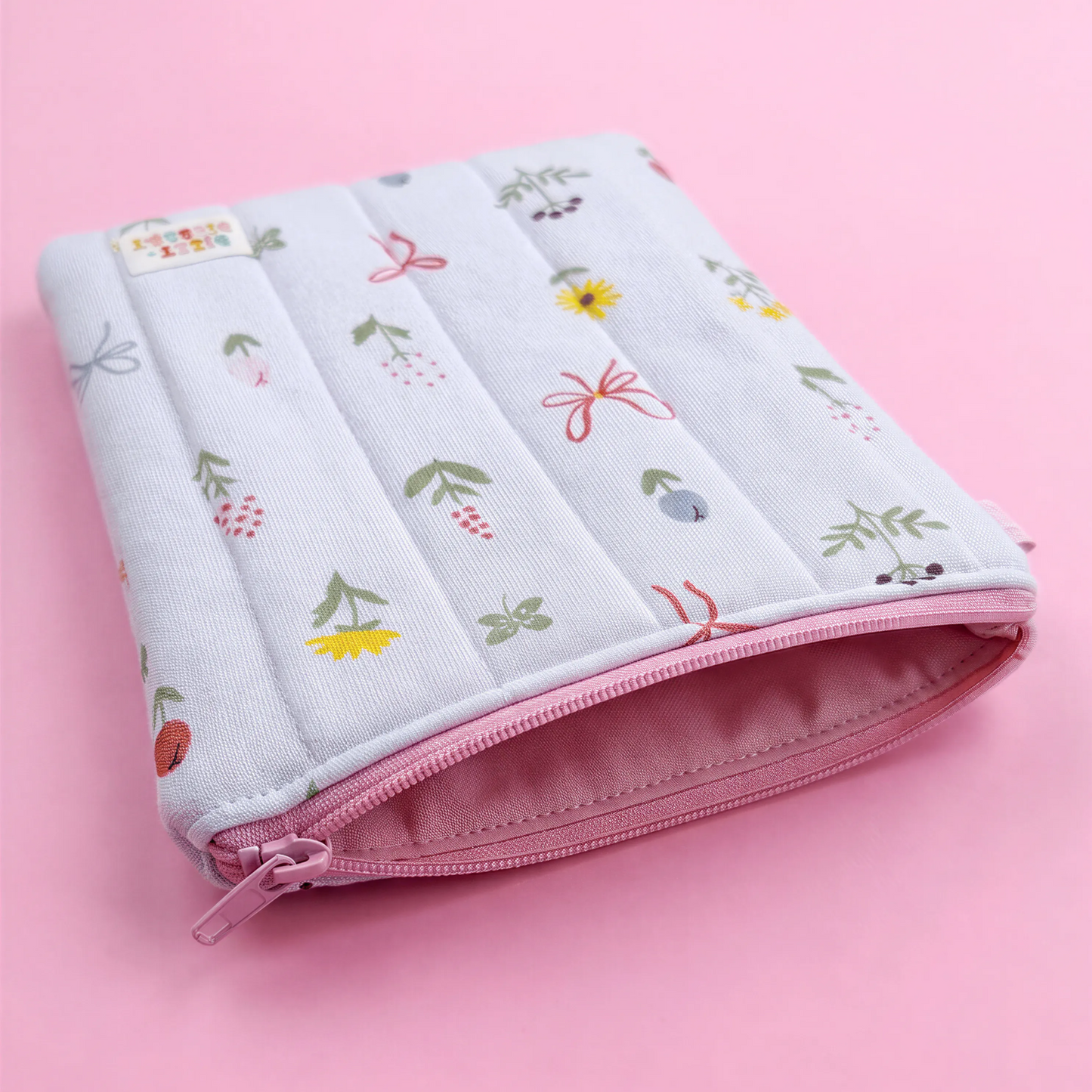 A white and pink floral patterned pouch with a zipper closure, resting on a pink background.
