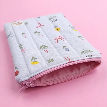 A white and pink floral patterned pouch with a zipper closure, resting on a pink background.