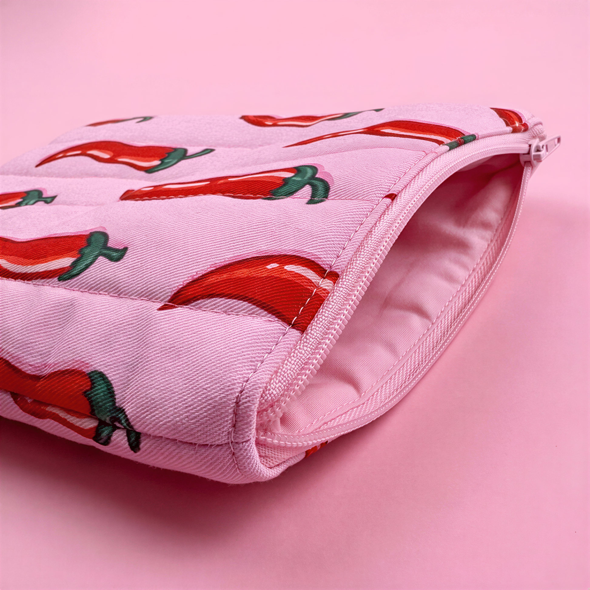 A pink zippered pouch with a repeating pattern of red chili peppers on a pink background.