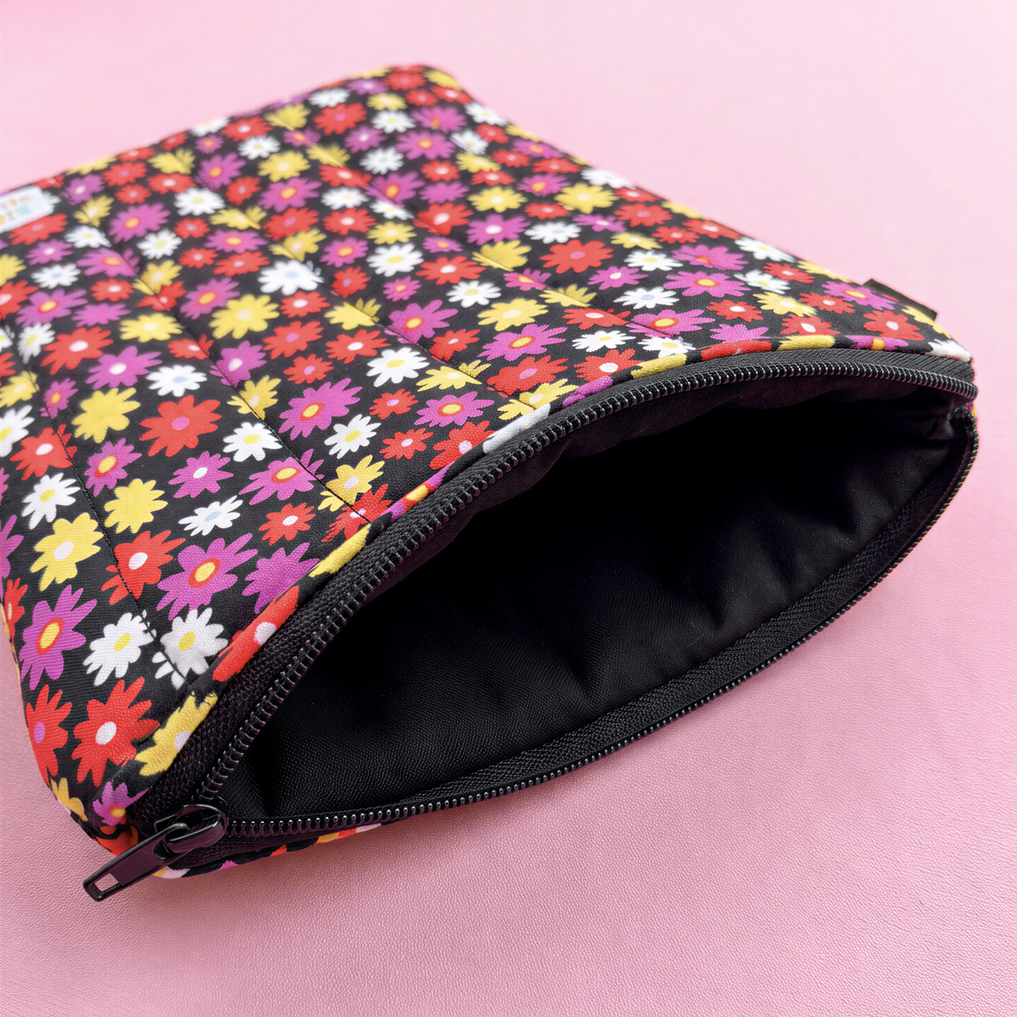 A colorful floral patterned pouch with a black zipper, resting on a pink surface.