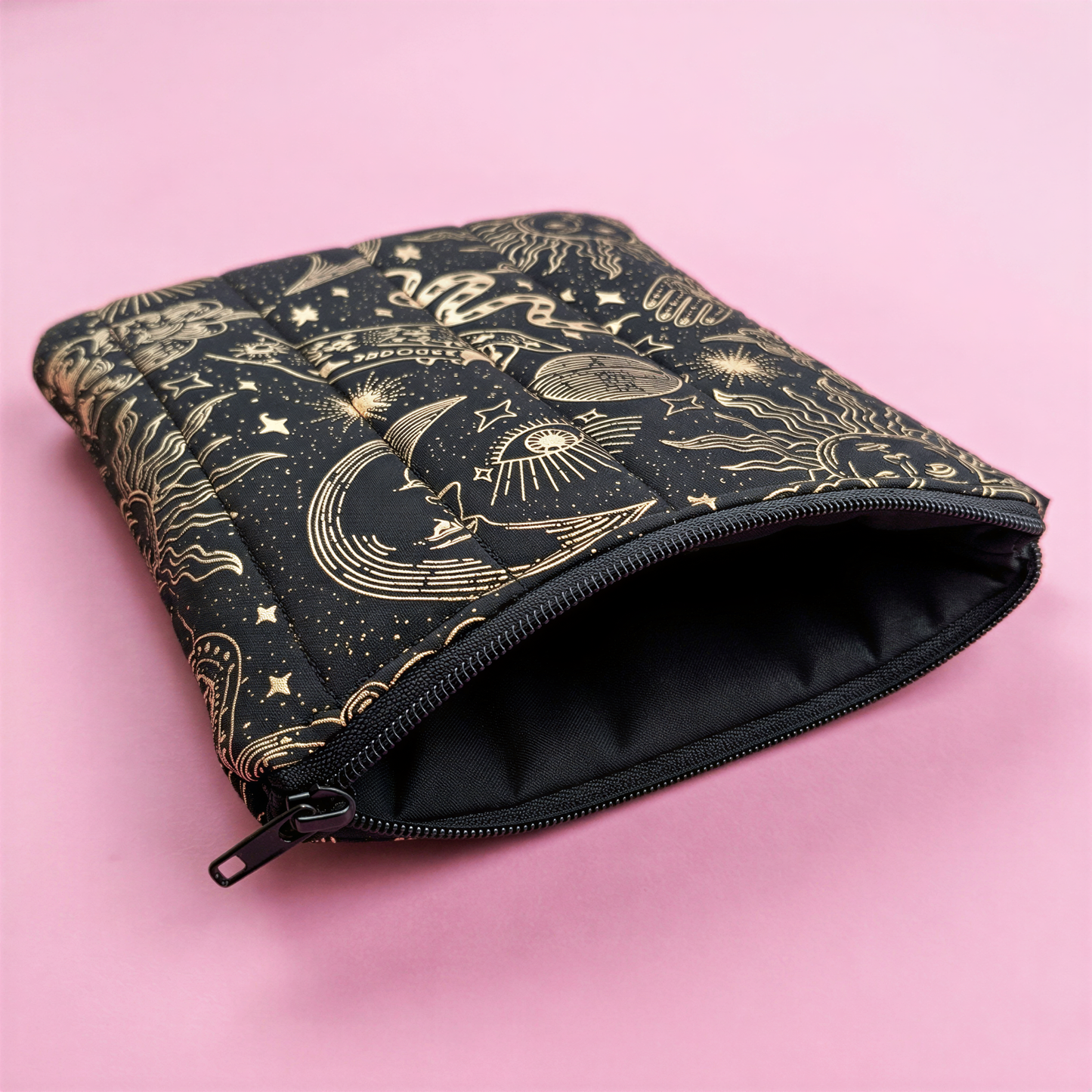 A black and gold zippered pouch with a starry night sky design on a pink background.