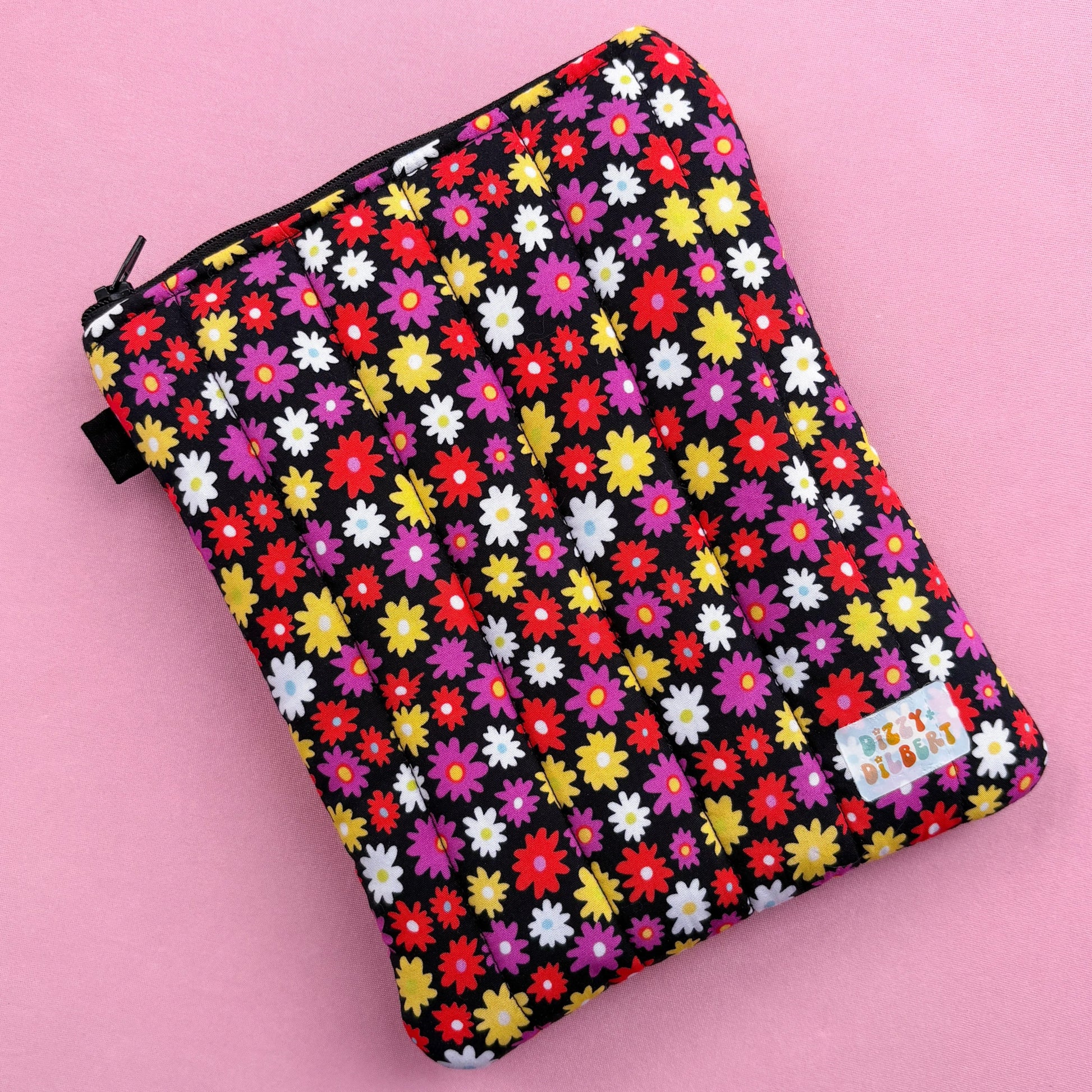 A colorful floral patterned bag or pouch with a vibrant design of various flowers in different colors, including red, yellow, and white, against a pink background.