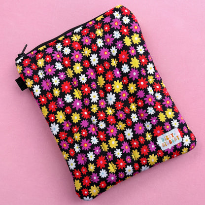 A colorful floral patterned bag or pouch with a vibrant design of various flowers in different colors, including red, yellow, and white, against a pink background.