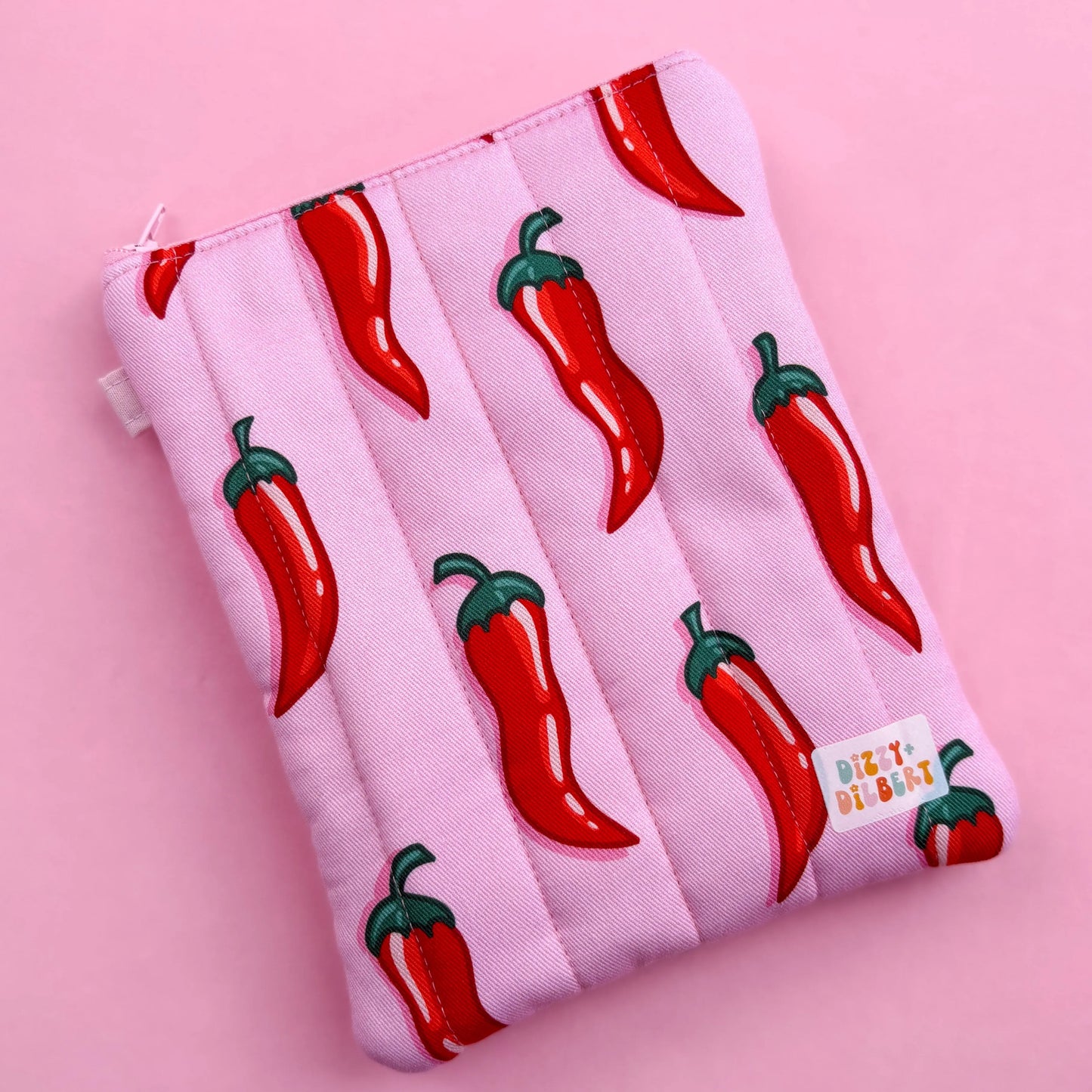 A pink pouch with a repeating pattern of red chili peppers on a pink background.