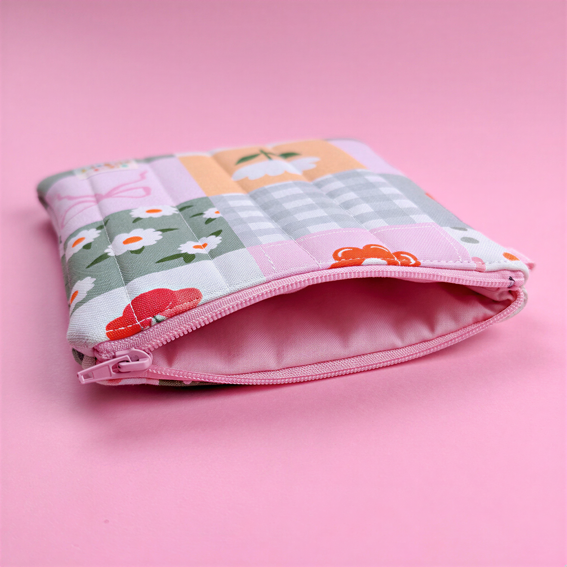 A colorful, patterned pouch with a floral design sits on a pink background.