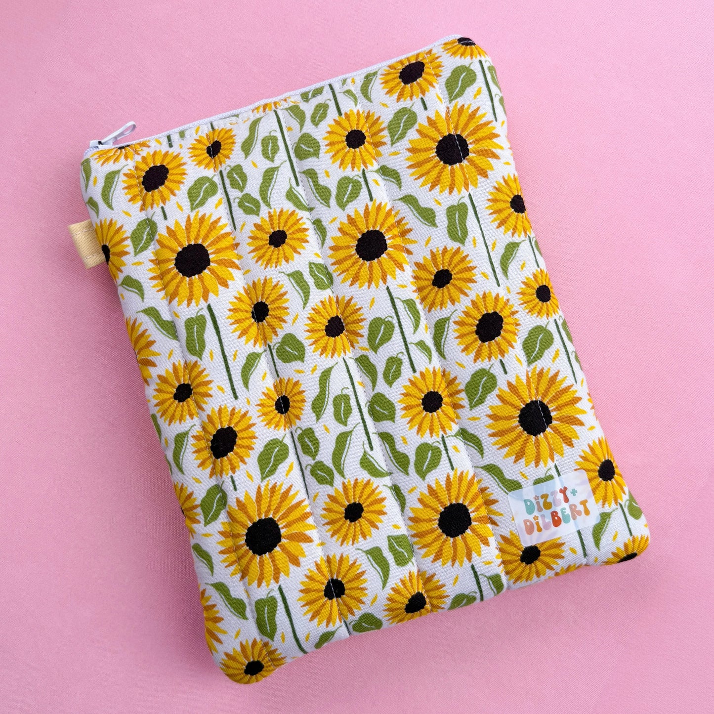 A white pouch with a yellow sunflower pattern printed on it, placed on a pink background.