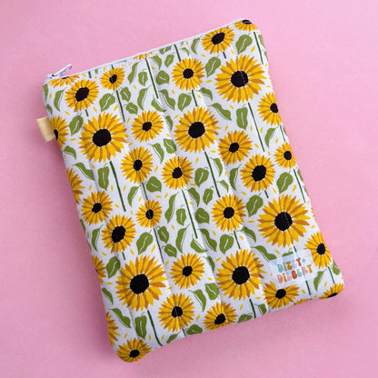 A white pouch with a yellow sunflower pattern printed on it, placed on a pink background.