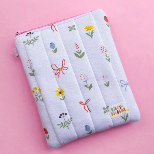 A white pouch with a floral pattern and colorful flowers printed on it, placed on a pink background.
